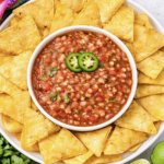 Fresh tomato salsa in a white bowl surrounded by tortilla chips on a bright kitchen counter.