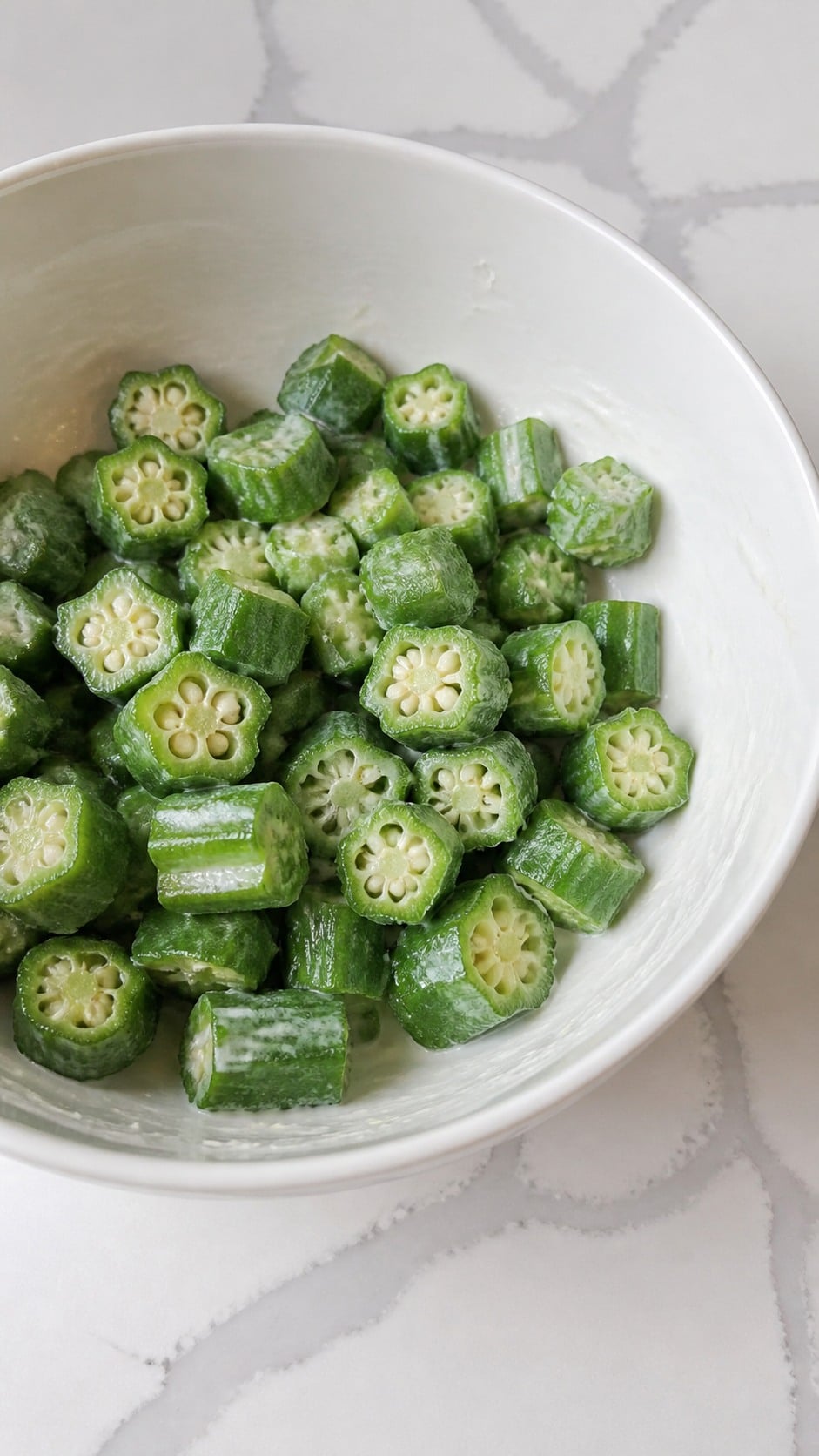Sliced okra lightly coated with buttermilk in a large bowl.