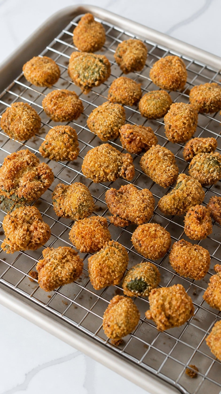 Deep golden fried okra draining on a wire rack after frying in small batches.