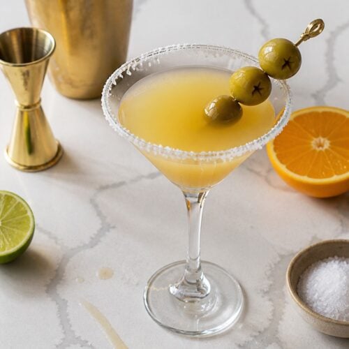 Overhead Mexican martini with a salted rim, three olives, citrus, coarse salt, and naturally worn gold barware.