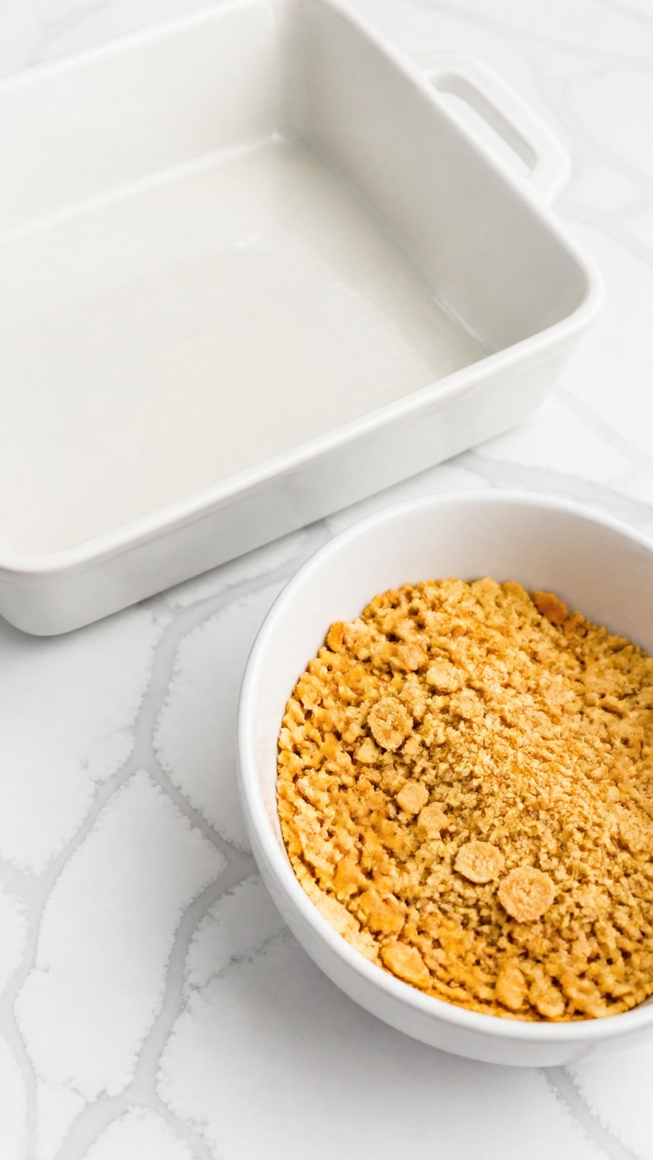 Crushed Ritz crackers in a mixing bowl beside a greased 9x13-inch baking dish.