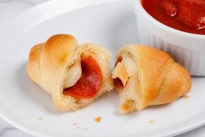 Pepperoni pizza crescent roll torn open to show mozzarella and pepperoni.