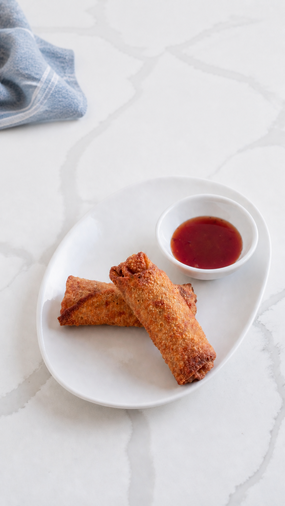 Overhead view of two homemade pork egg rolls with sweet and sour sauce on a white quartz counter.