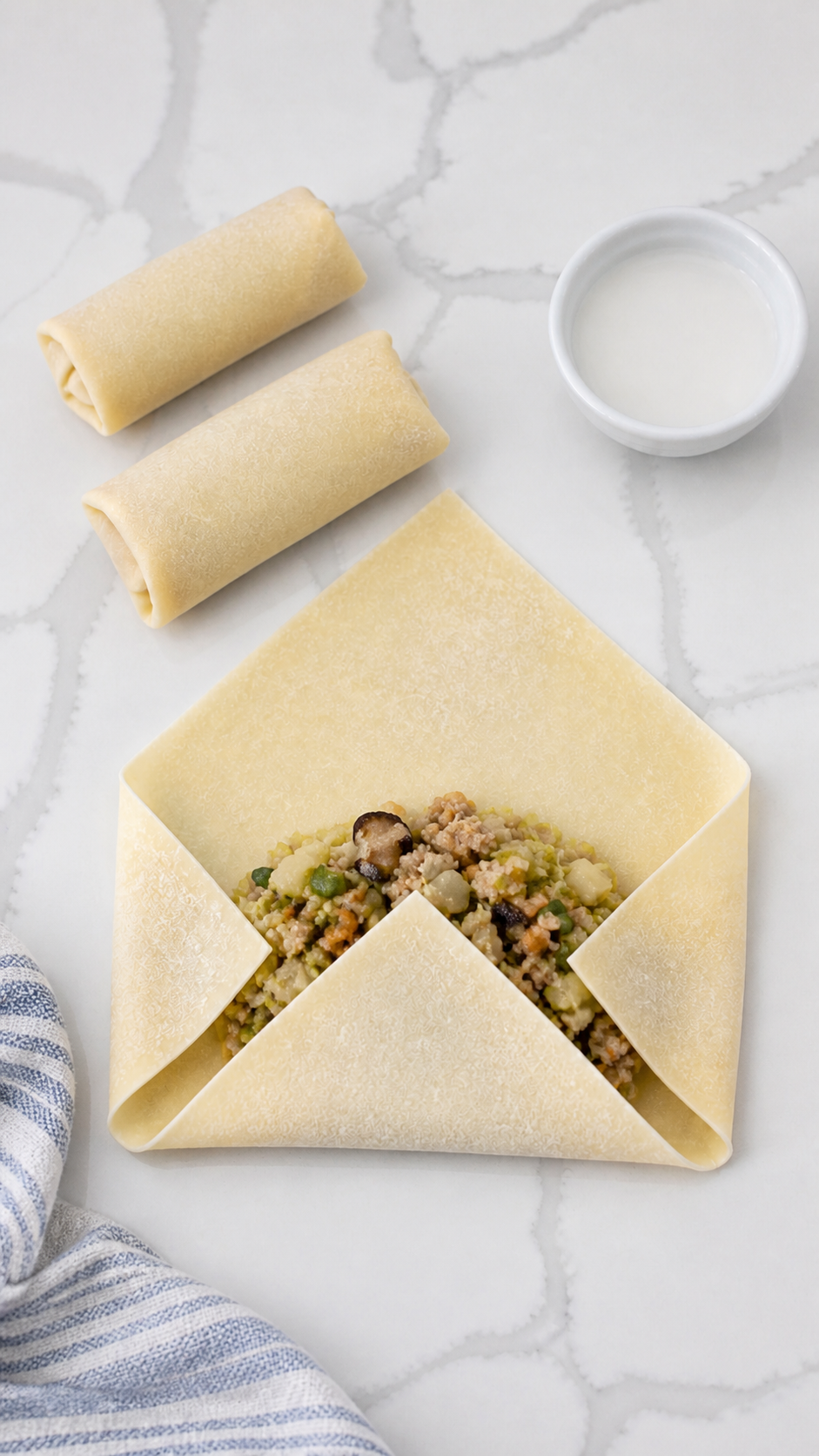 An egg roll wrapper folded around pork and vegetable filling with slurry ready for sealing.
