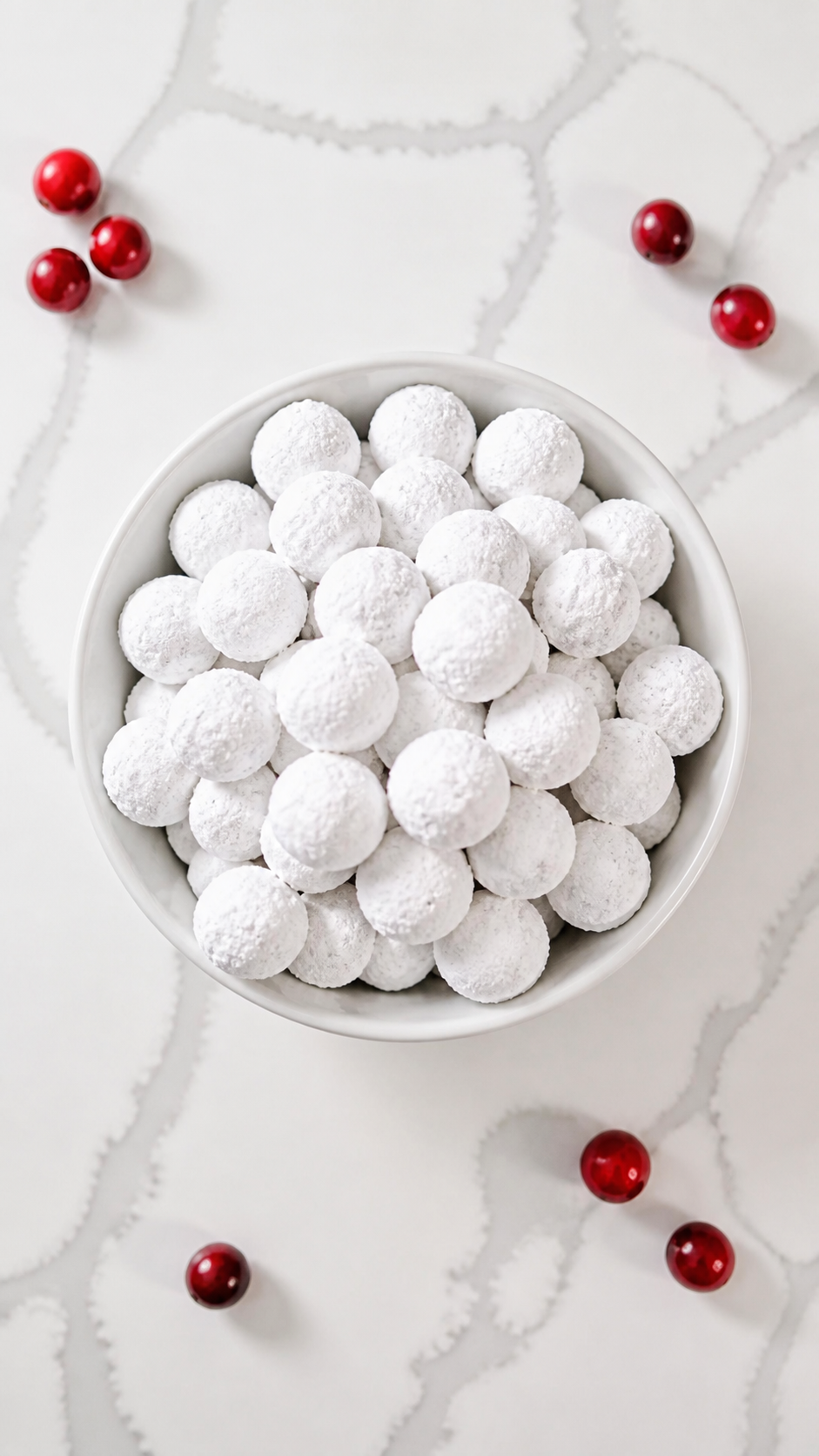 Overhead bowl of whole powdered sugar cranberry snowballs on a bright white counter.