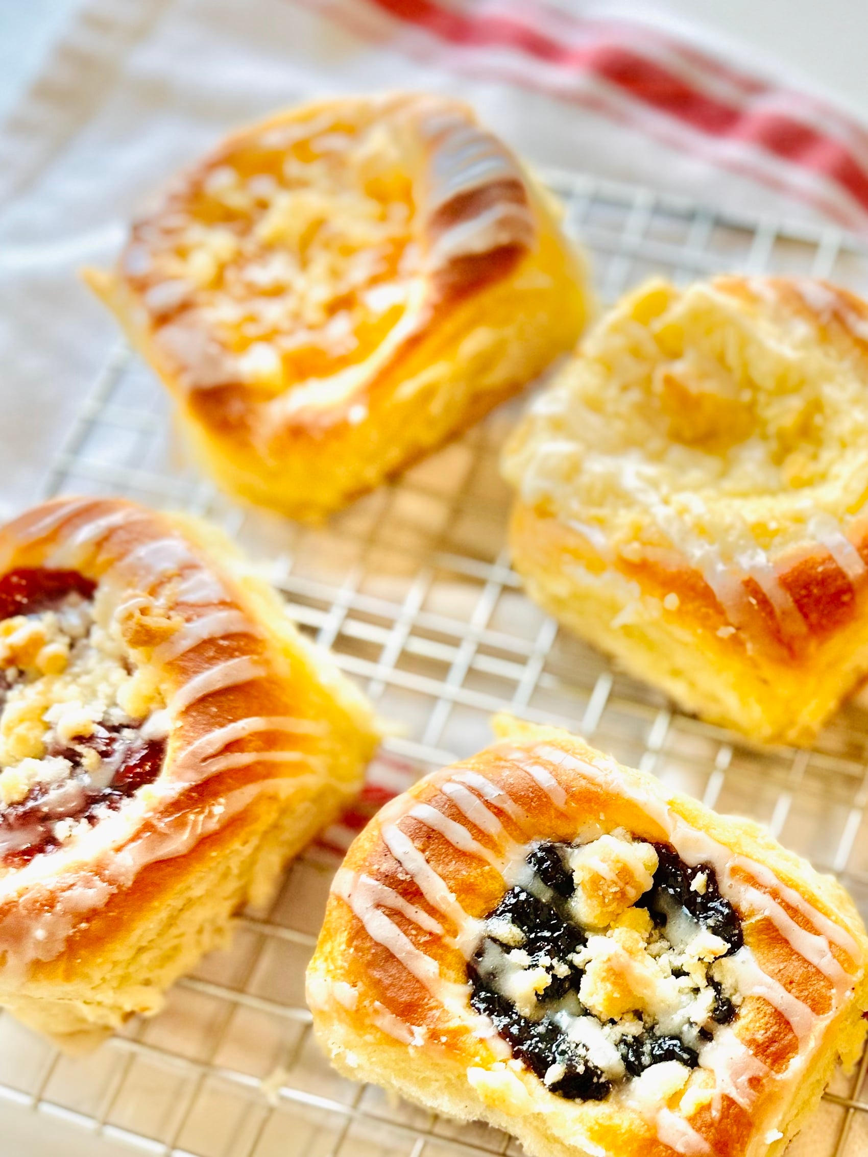 Close-up of a blueberry kolache with posypka and vanilla icing on a cooling rack.