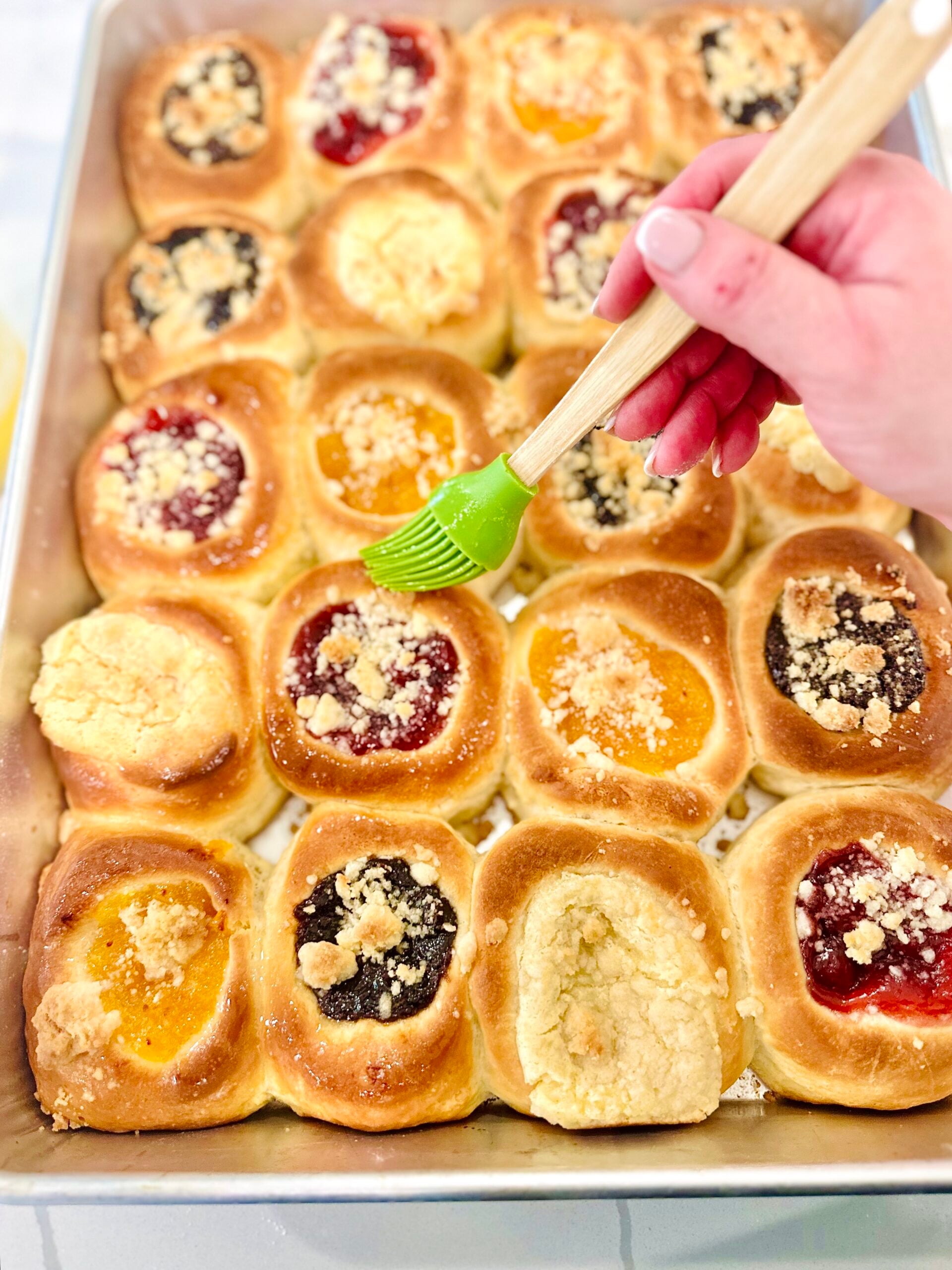 Freshly baked Texas Czech kolaches being brushed with melted butter in the baking pan.