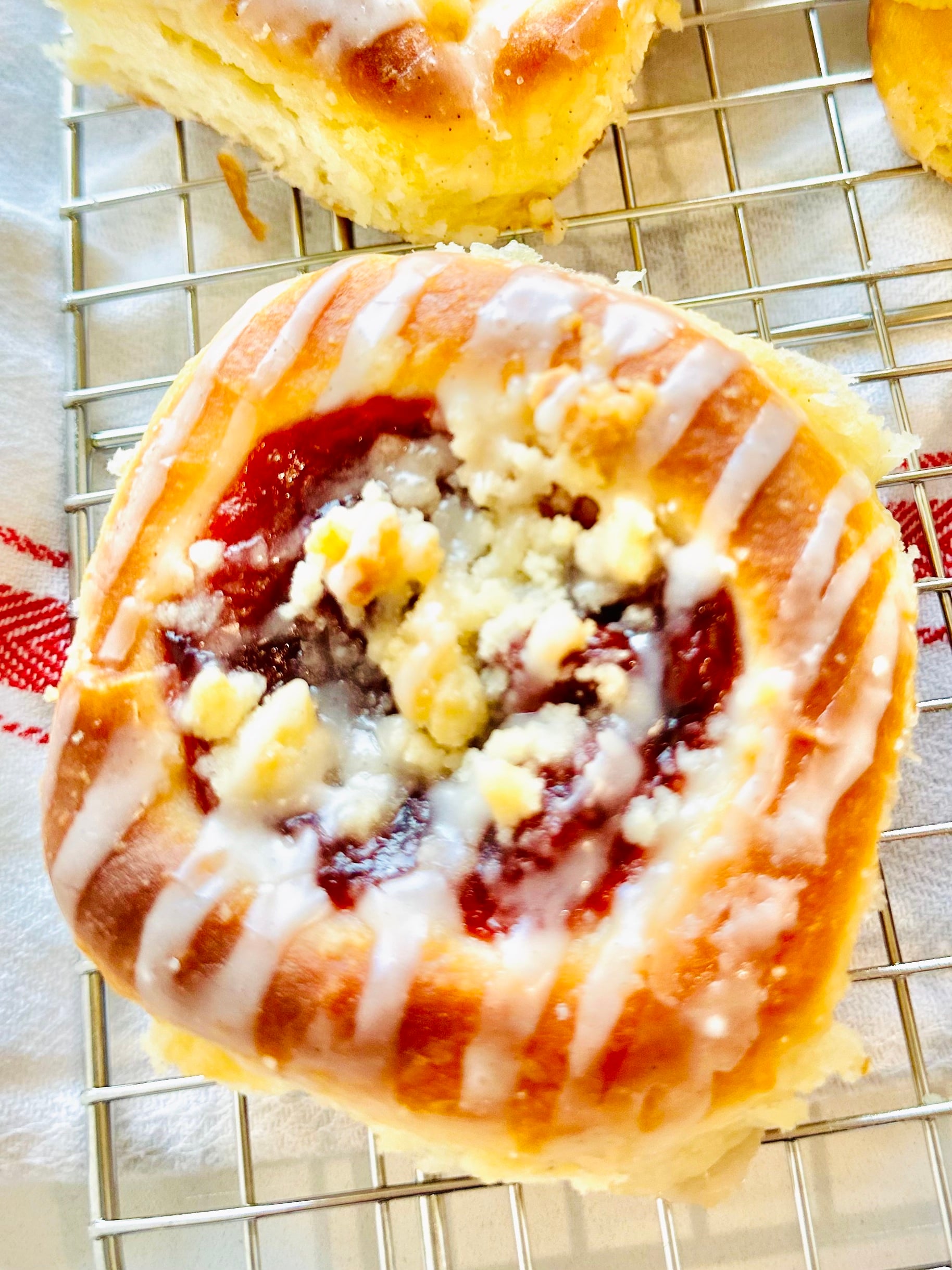 Close-up of a cherry kolache topped with posypka and vanilla icing.