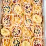 Overhead pan of homemade Texas Czech kolaches with assorted fruit, poppy seed, cream cheese, posypka, and vanilla icing.