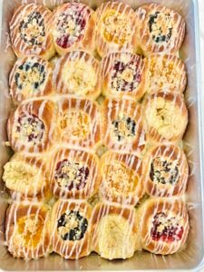 Overhead pan of homemade Texas Czech kolaches with assorted fruit, poppy seed, cream cheese, posypka, and vanilla icing.