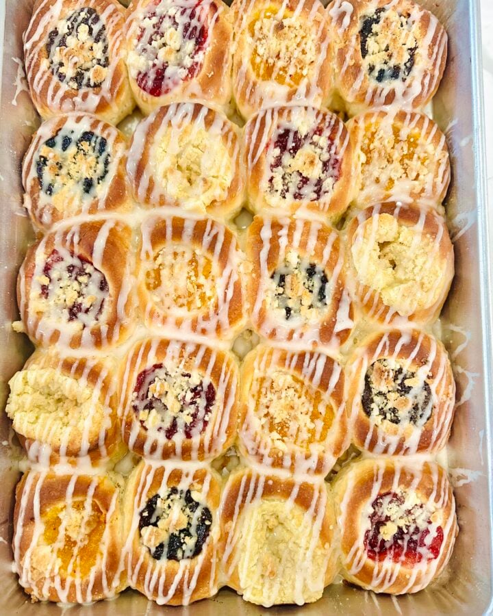 Overhead pan of homemade Texas Czech kolaches with assorted fruit, poppy seed, cream cheese, posypka, and vanilla icing.