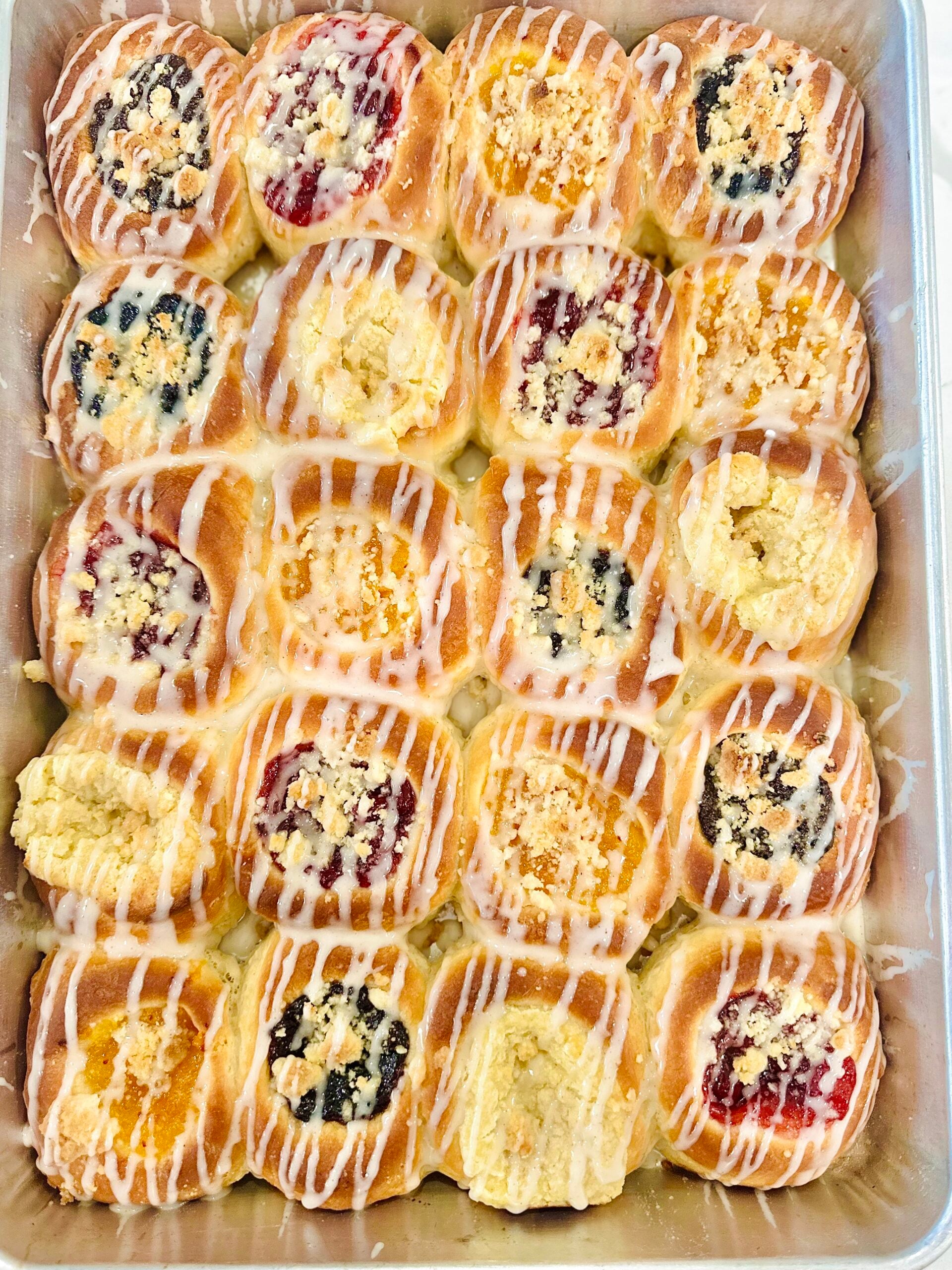Overhead pan of homemade Texas Czech kolaches with assorted fruit, poppy seed, cream cheese, posypka, and vanilla icing.