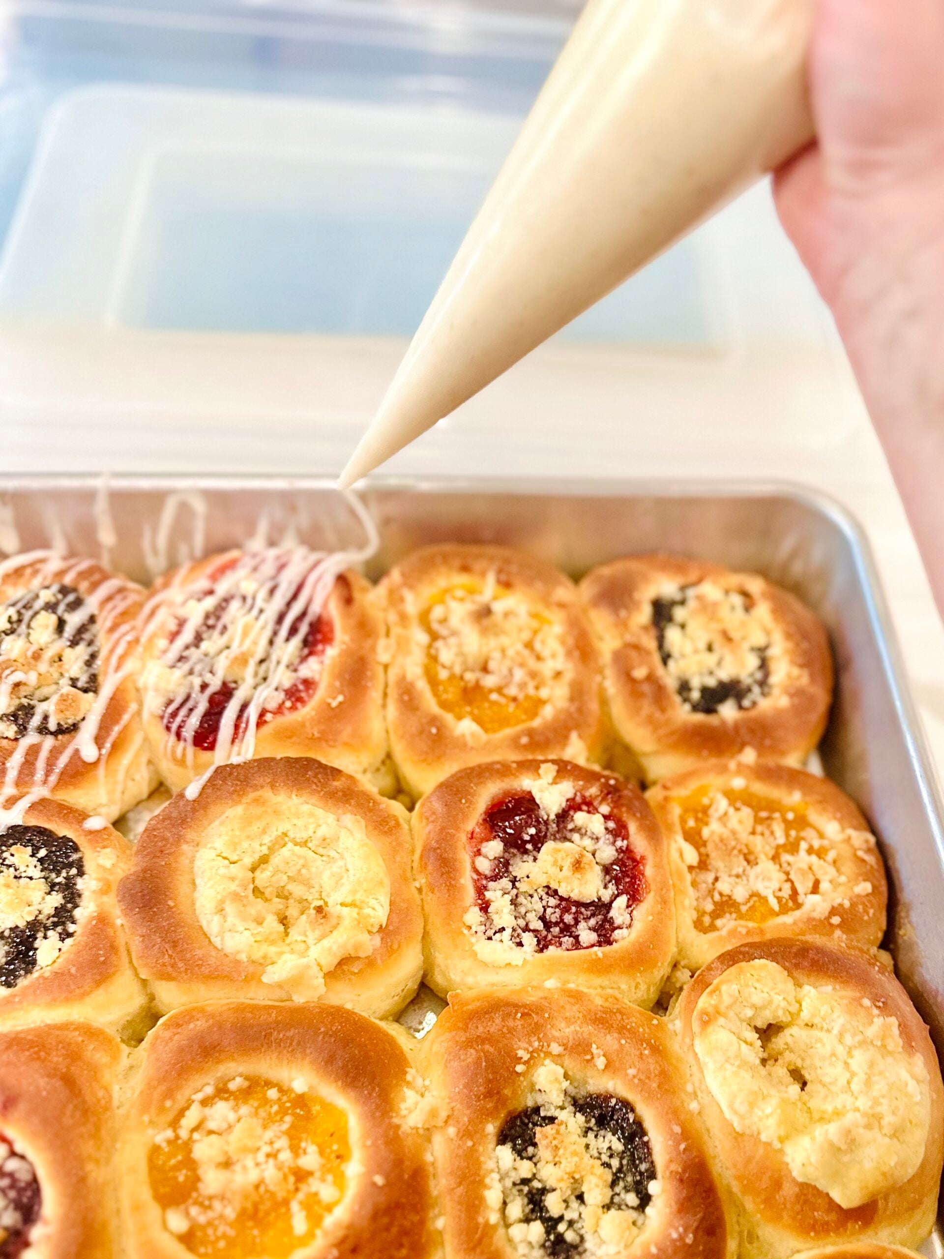 Vanilla icing being drizzled over a pan of homemade Texas Czech kolaches.