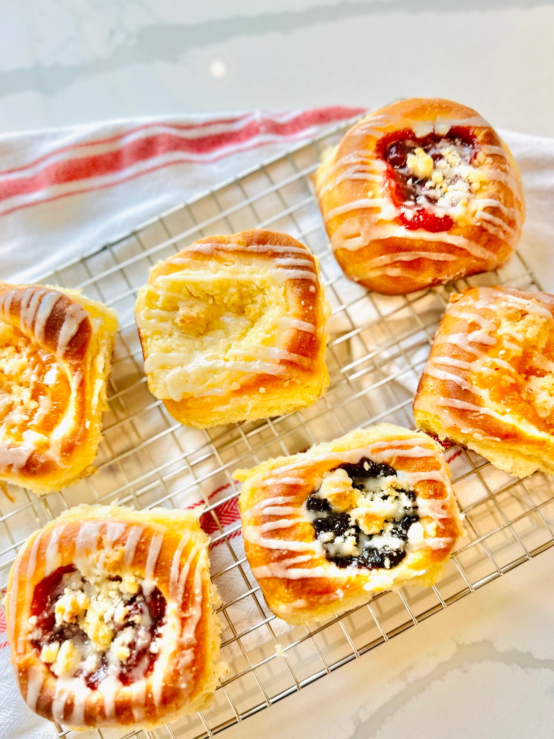 Assorted homemade Texas Czech kolaches with fruit and cream cheese fillings on a cooling rack.