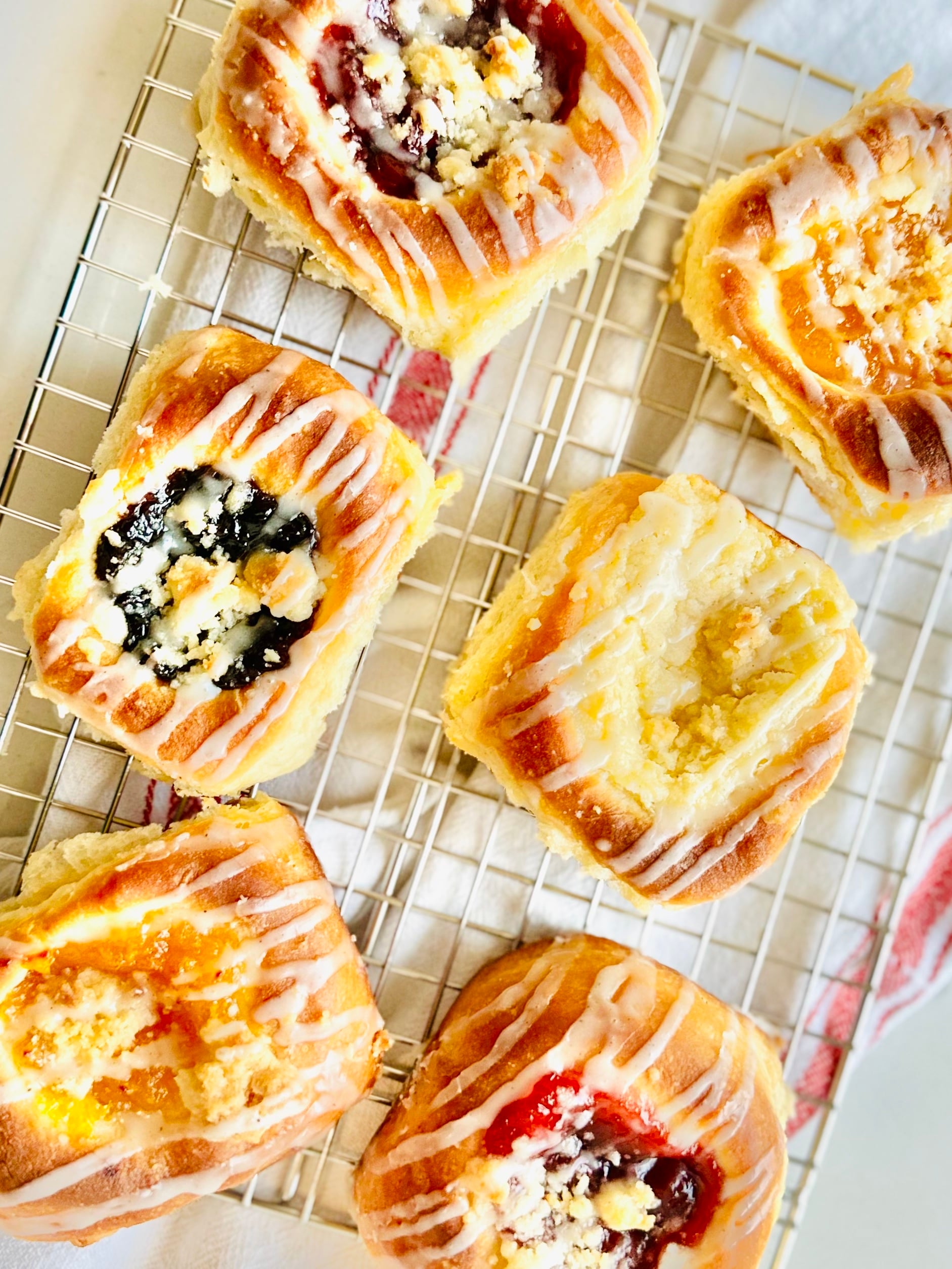 Assorted fruit, poppy seed, and cream cheese kolaches cooling on a wire rack.