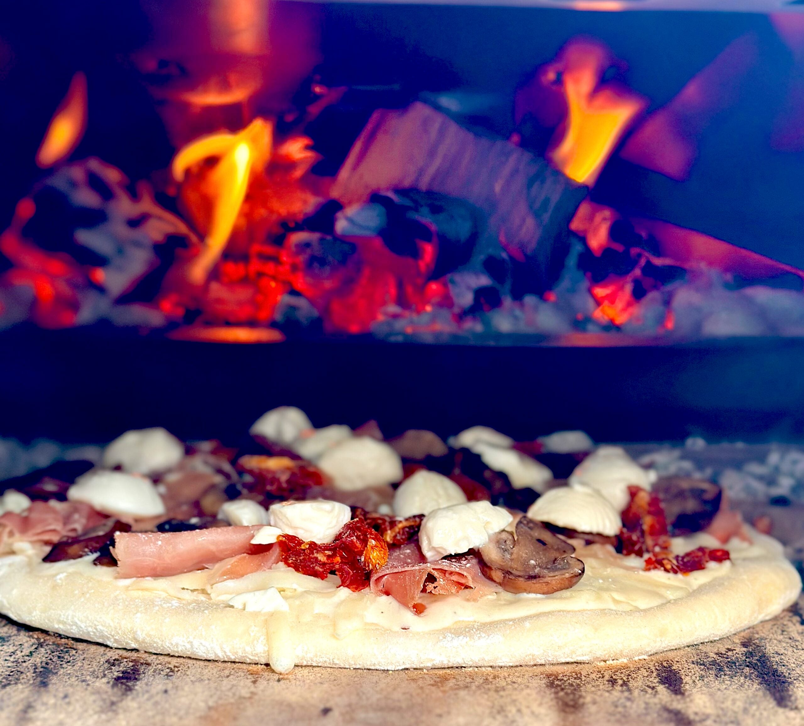 Topped pizza entering a flaming Ooni Karu 2 Pro Multi-Fuel Pizza Oven before baking.