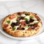 Wood-fired pizza with a puffy blistered crust made from overnight poolish dough.