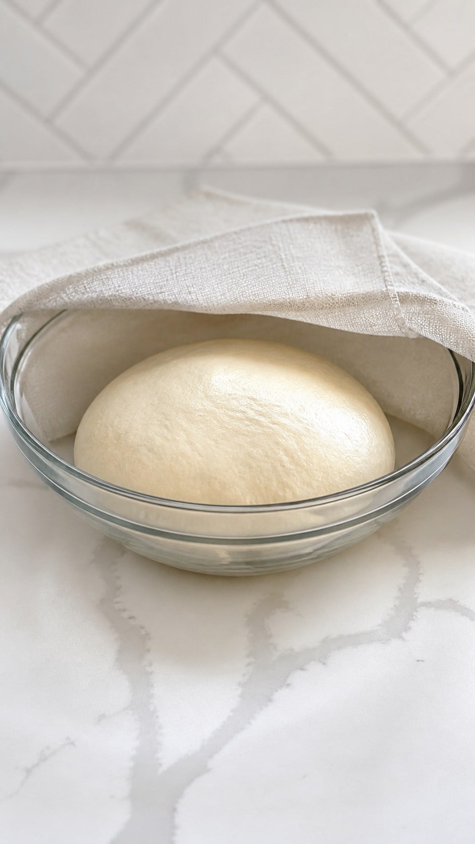 Pizza dough resting in a lightly oiled glass bowl.