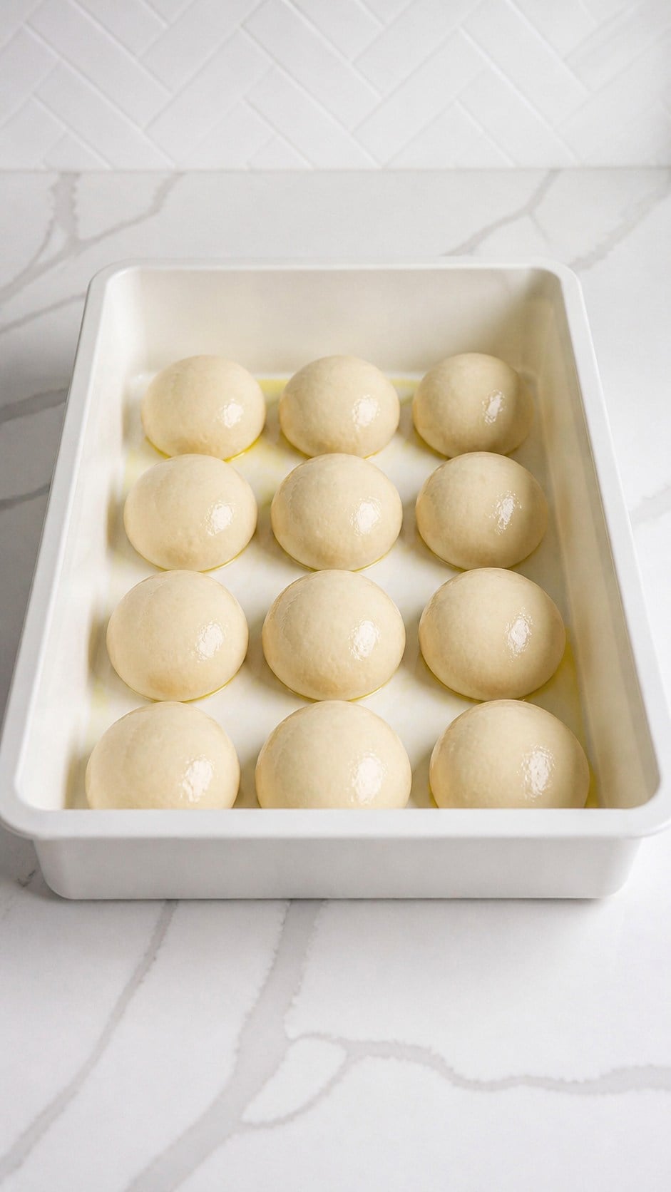 Twelve smooth pizza dough balls arranged in a proofing box.