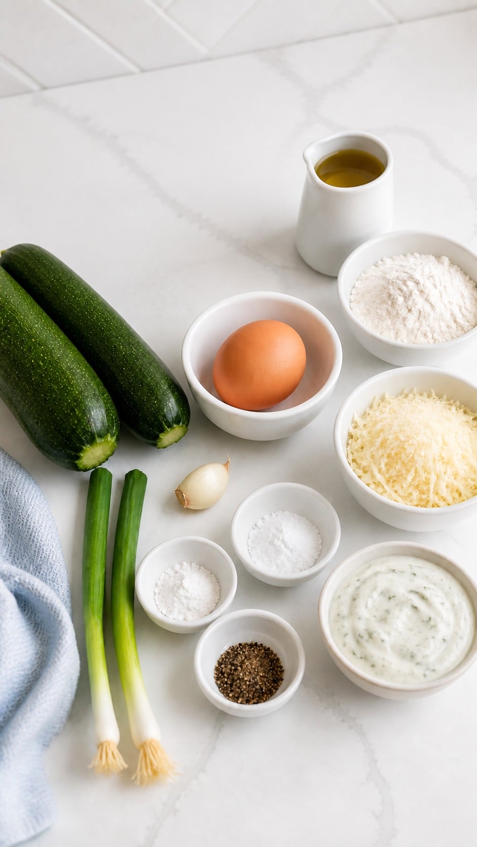 Zucchini, egg, green onions, Parmesan, garlic, flour, baking powder, pepper, salt, and olive oil arranged for zucchini fritters.