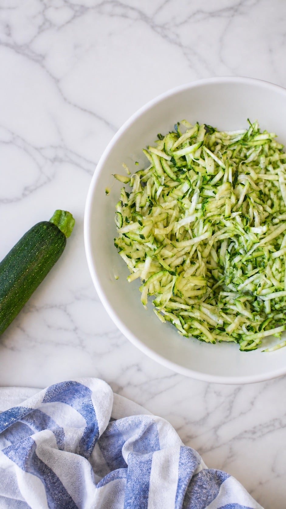 Grated zucchini tossed with kosher salt and resting in a bowl to release moisture.