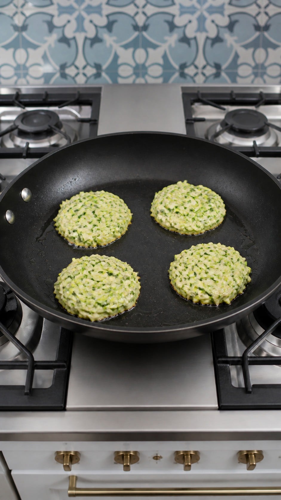 Half-inch-thick zucchini fritters browning in olive oil in a nonstick skillet.