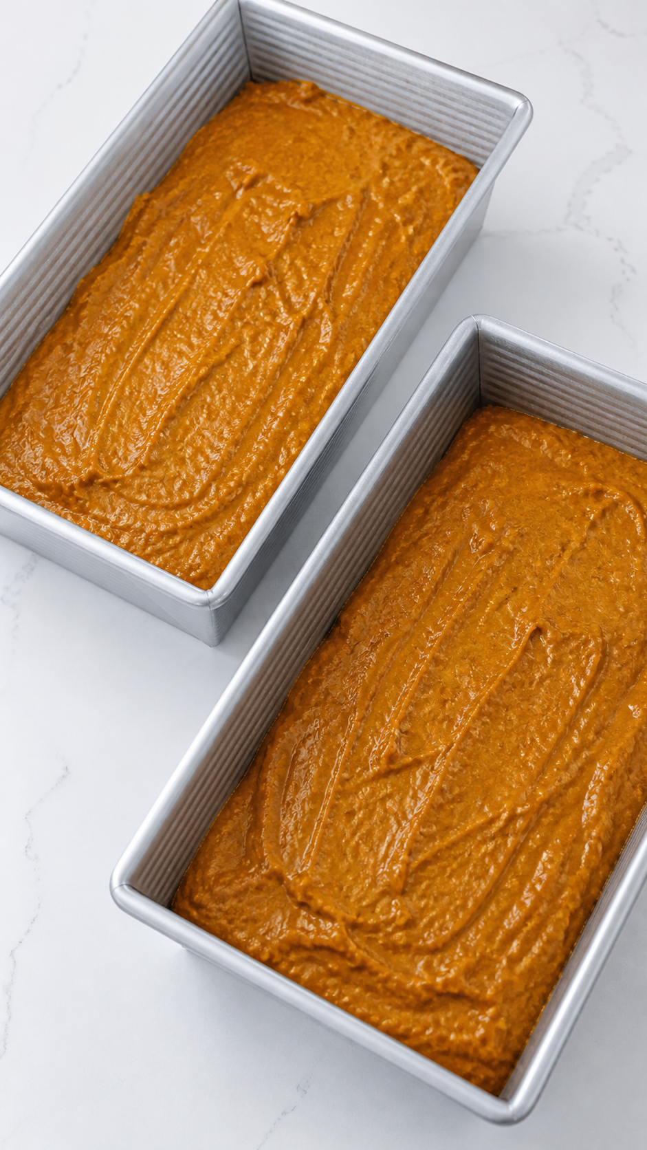 Pumpkin bread batter divided evenly between two loaf pans