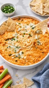 Tortilla chip lifting buffalo chicken dip with ranch, shredded chicken, melted cheese, and blue cheese crumbles.