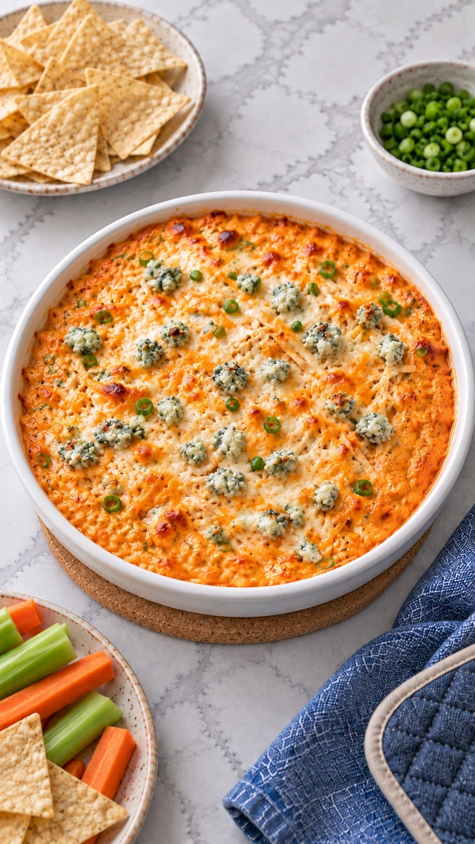 Baked buffalo chicken dip with melted cheese and lightly browned spots in a round white ceramic dish.