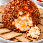 Finished pecan-coated cheese ball with crackers and appetizer accompaniments.