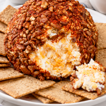 Pecan-coated cheddar cheese ball with a scoop removed to show the creamy four-cheese filling.