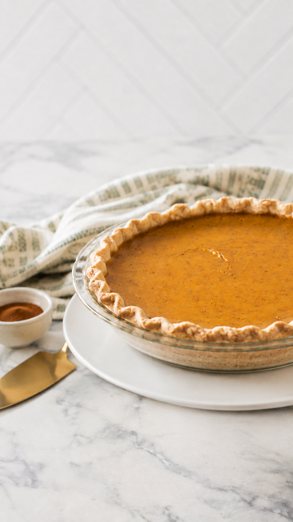 Whole classic pumpkin pie in a glass pie dish on a white porcelain plate from a low diagonal angle.