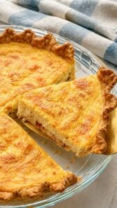 A creamy bacon and Gruyère Quiche Lorraine wedge with a naturally uneven cut and flaky crumbs on a gold pie server.