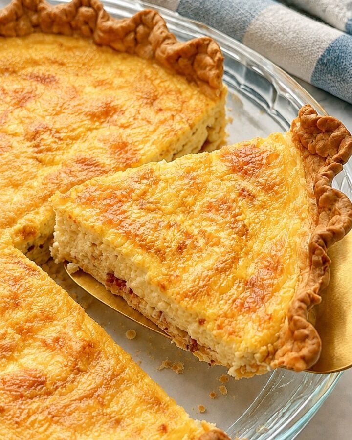 A creamy bacon and Gruyère Quiche Lorraine wedge with a naturally uneven cut and flaky crumbs on a gold pie server.