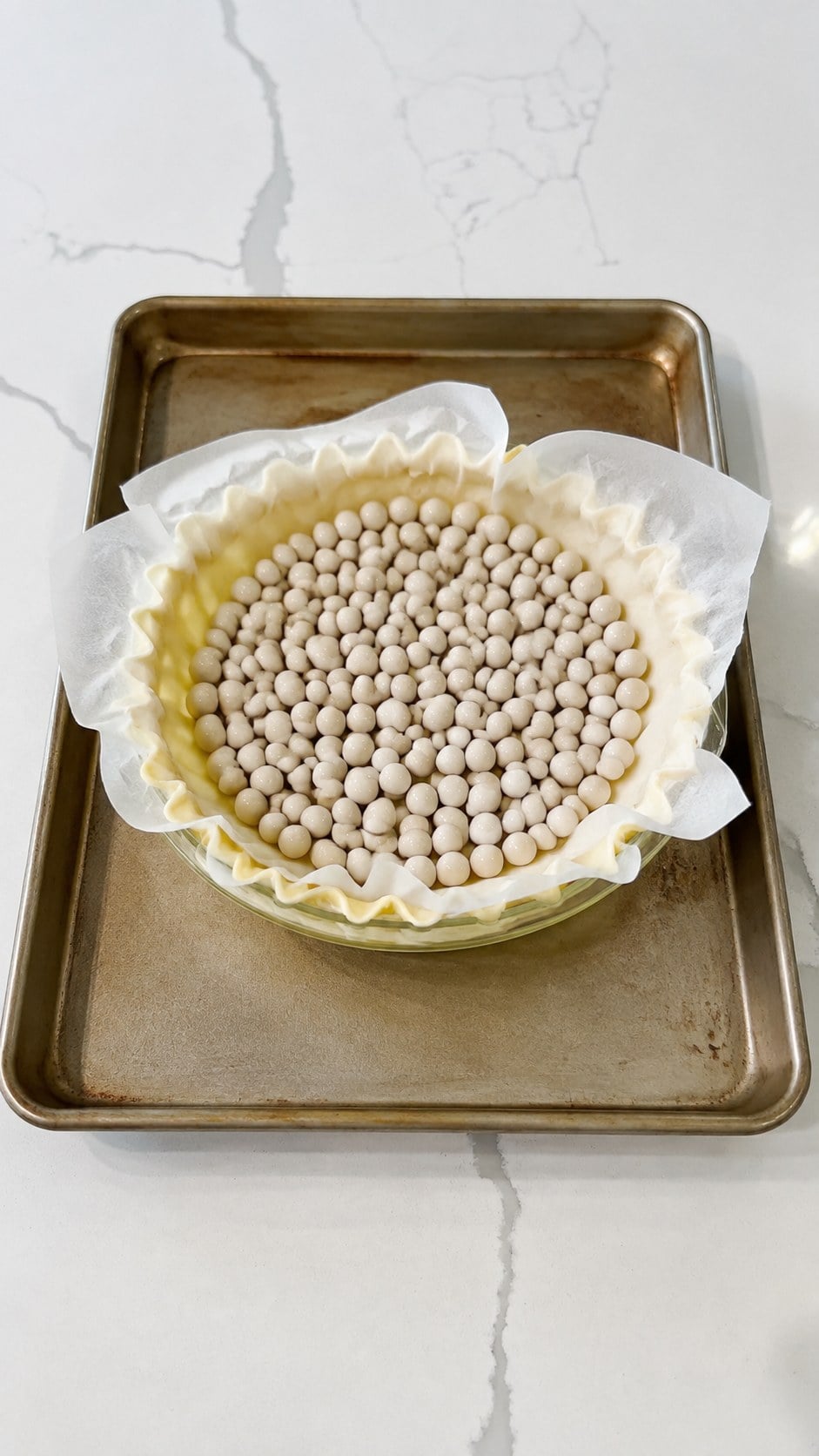 Crimped pie crust lined with parchment and pie weights on a baking sheet for blind baking.