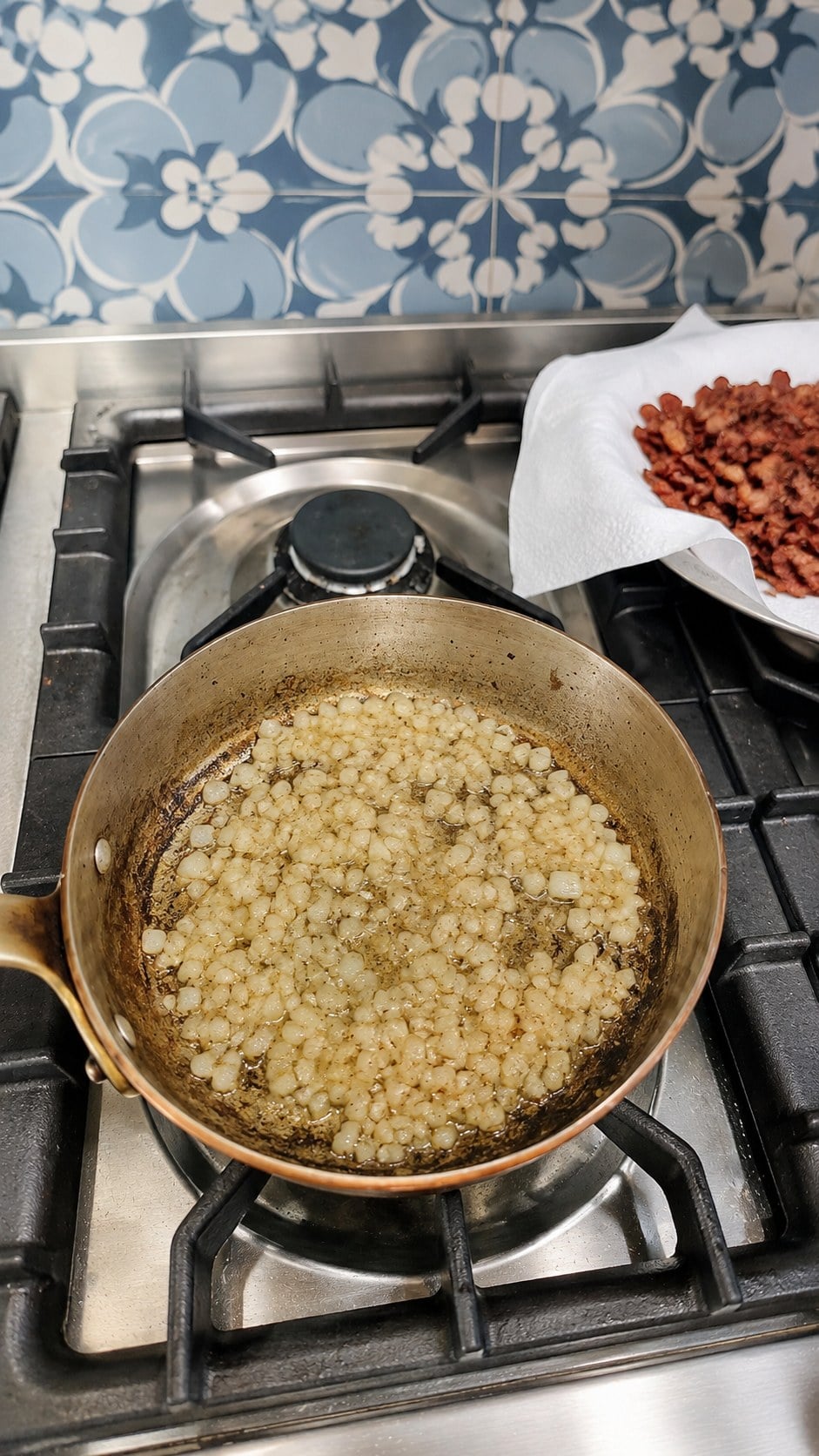 Diced onions cooking in bacon drippings while crisp bacon drains on paper towels.
