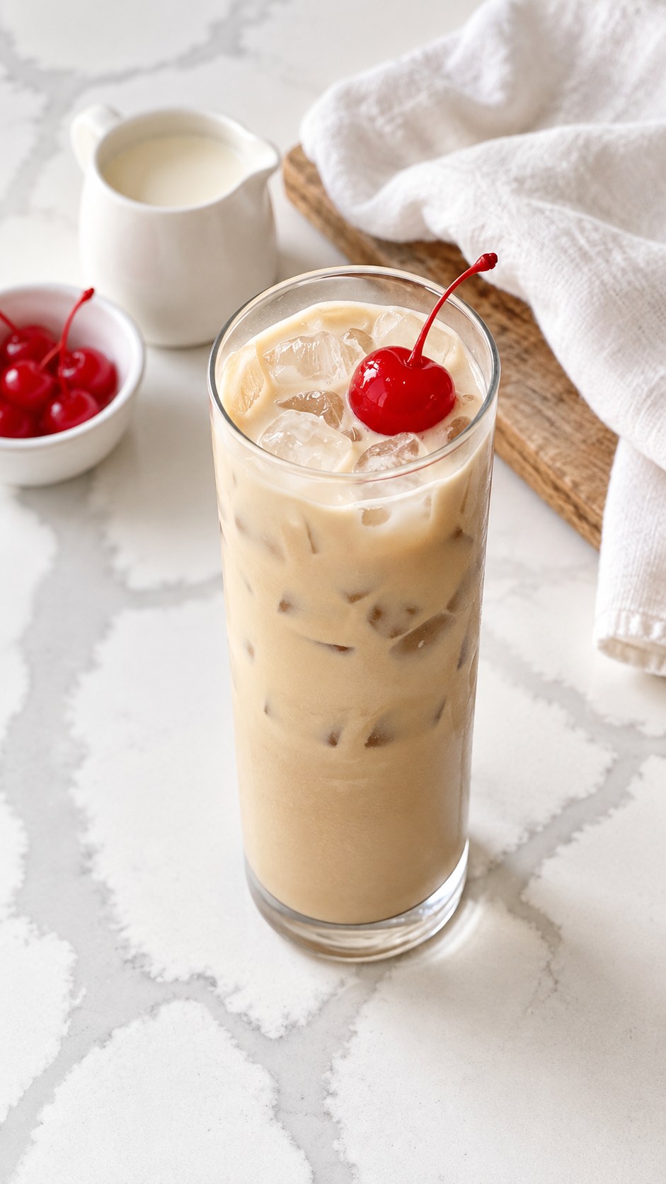 Overhead angled view of a creamy Colorado Bulldog with a cream pitcher and cherries nearby.