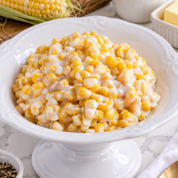 Creamed corn with cream cheese in a white serving bowl with fresh corn and cream nearby.
