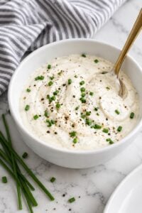 Creamy horseradish sauce topped with chives and black pepper in a plain white ceramic bowl.