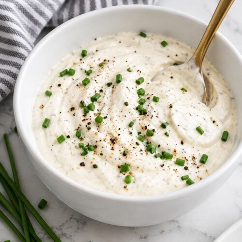 Creamy horseradish sauce topped with chives and black pepper in a plain white ceramic bowl.
