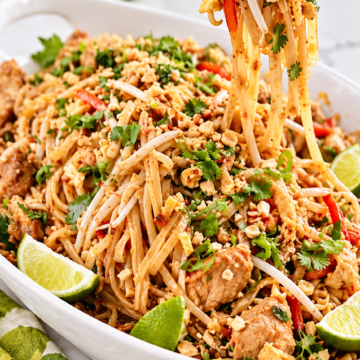 Wooden chopsticks lifting chicken Pad Thai noodles with chicken, red pepper, and peanuts.