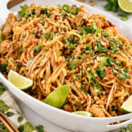 Easy chicken Pad Thai with red bell pepper, peanuts, cilantro, and lime on a white platter.