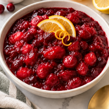 Baked cranberry sauce topped with thin orange slices and curled orange zest in an ivory bowl