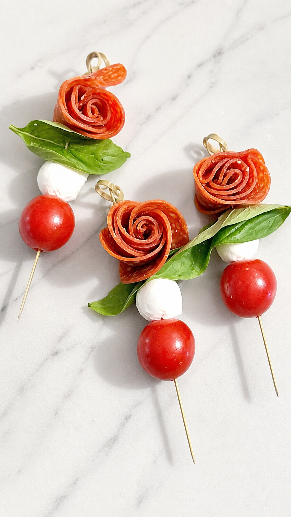 Pepperoni rose caprese skewers with basil, mozzarella pearls, and cherry tomatoes.