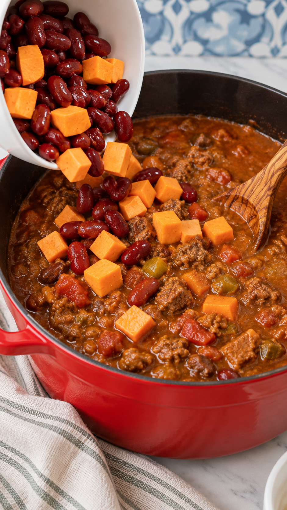 Kidney beans and diced sweet potatoes being added to beef chili