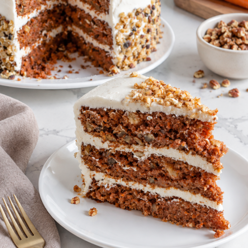 Three-layer carrot cake with cream cheese frosting and pecans beside a plated slice.