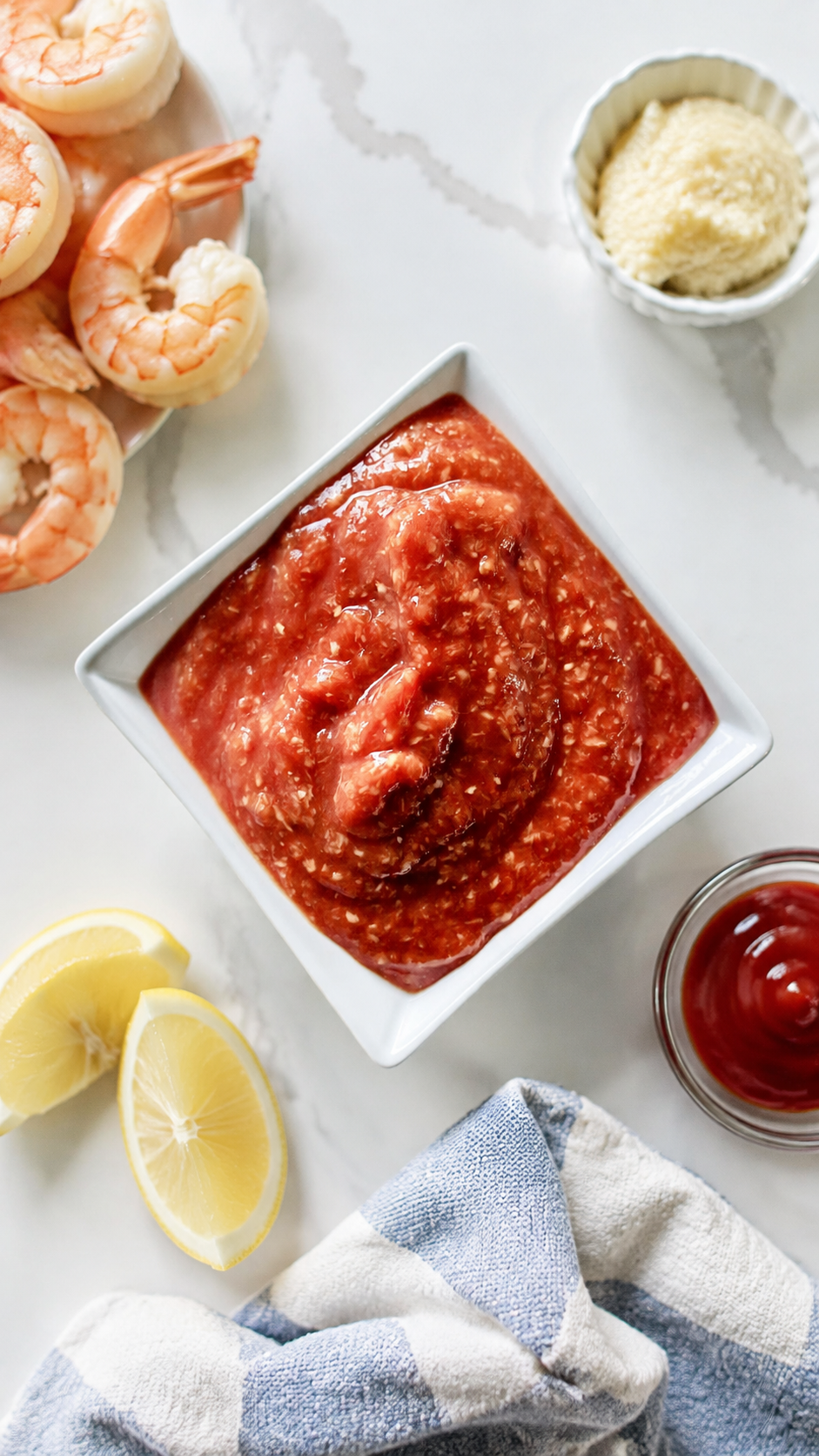 Overhead bowl of homemade cocktail sauce with shrimp, lemon, ketchup, and prepared horseradish