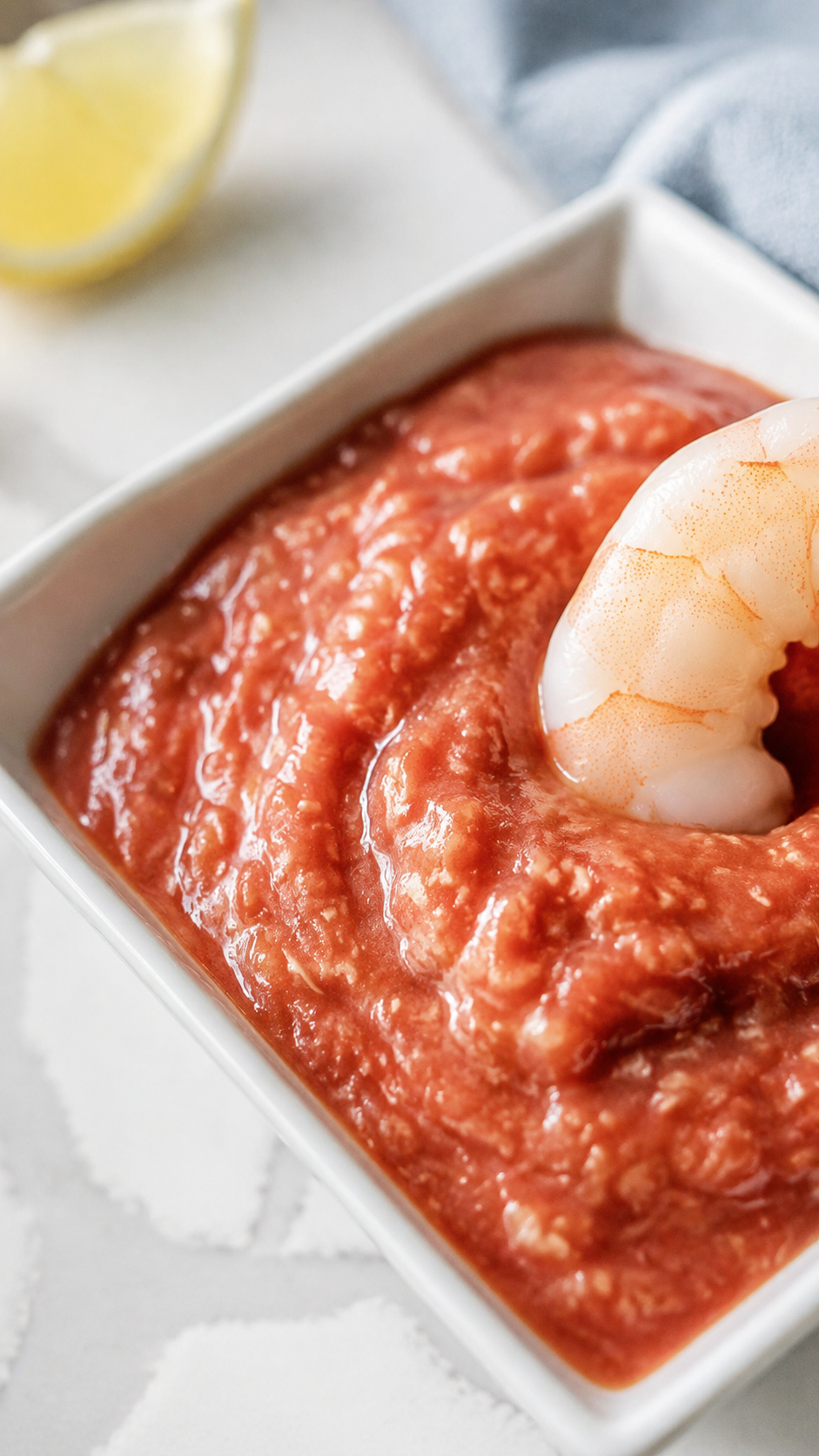 Close-up of homemade cocktail sauce with visible horseradish and a shrimp dipping into the bowl