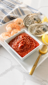 Homemade cocktail sauce served cold with boiled shrimp, oysters, and lemon wedges