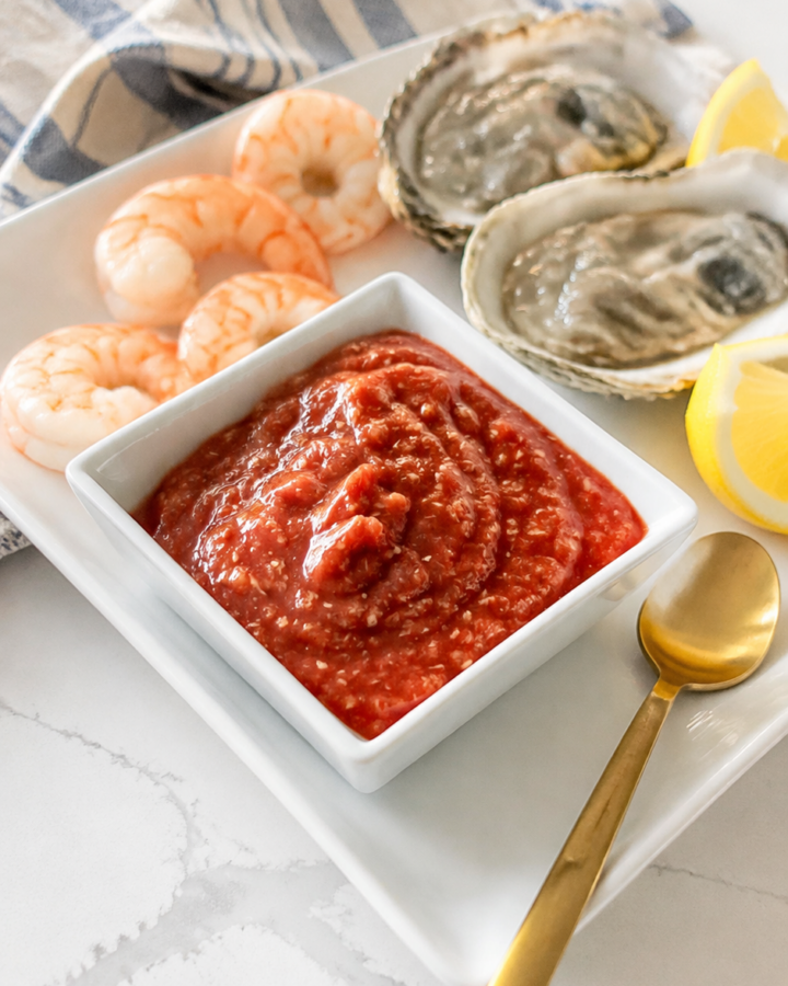 Homemade cocktail sauce served cold with boiled shrimp, oysters, and lemon wedges